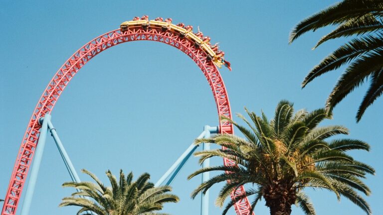 picture of a red and yellow rollercoaster at Movie World, a Gold Coast theme park against a blue sky with palms